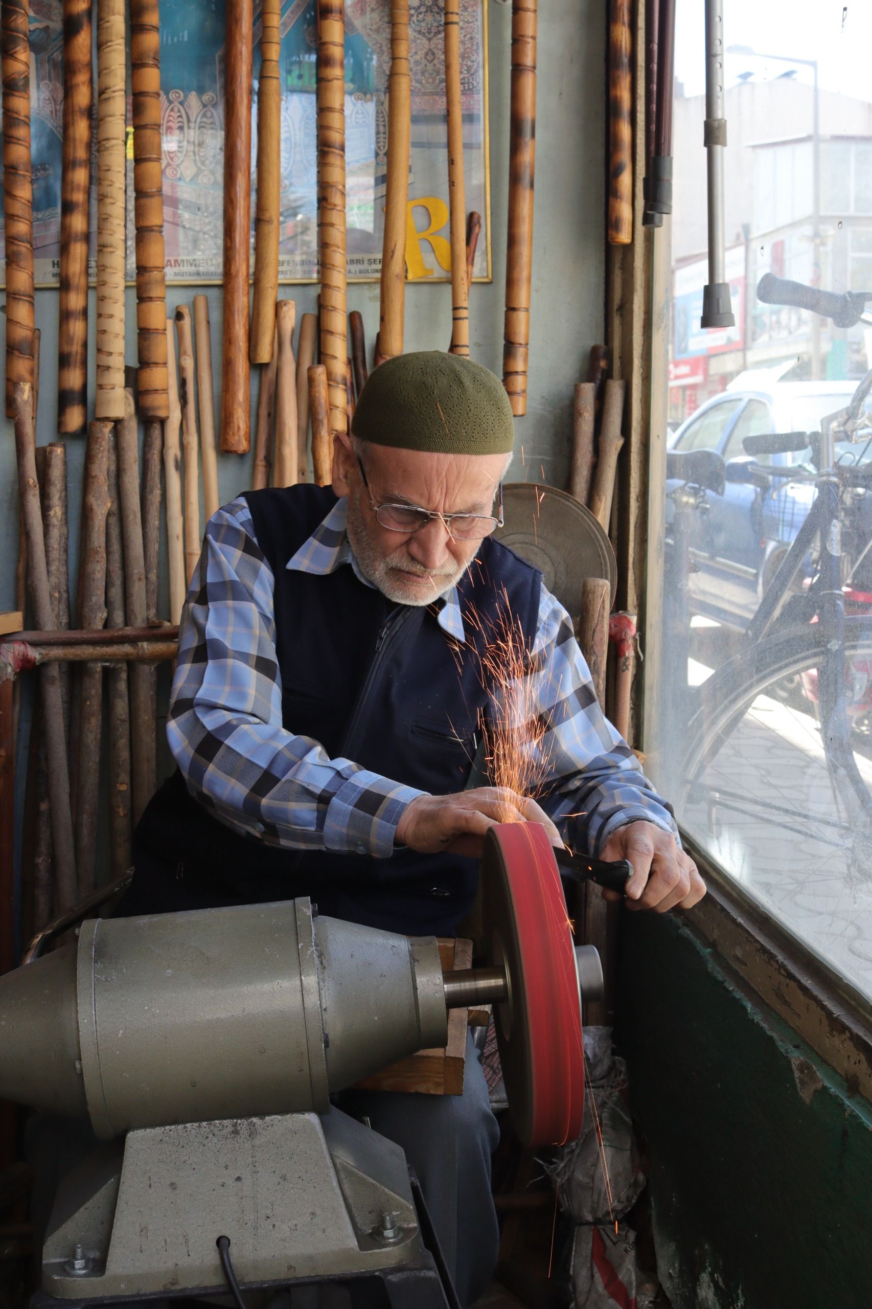 Elderly man sharpening tools on a grinding wheel in a sunlit workshop.