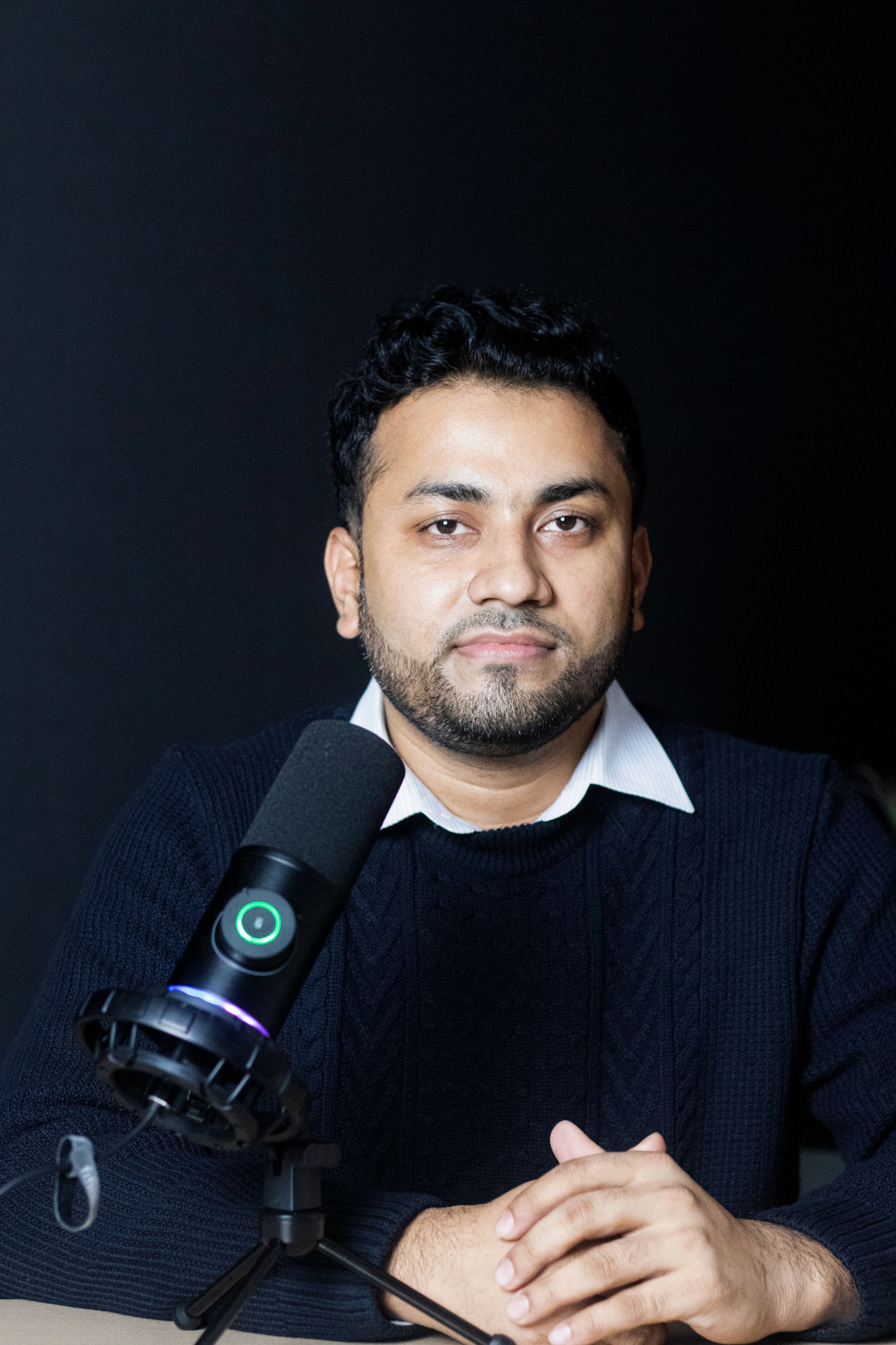 A South Asian man speaks into a microphone in a modern office setting, showcasing a professional podcast session.