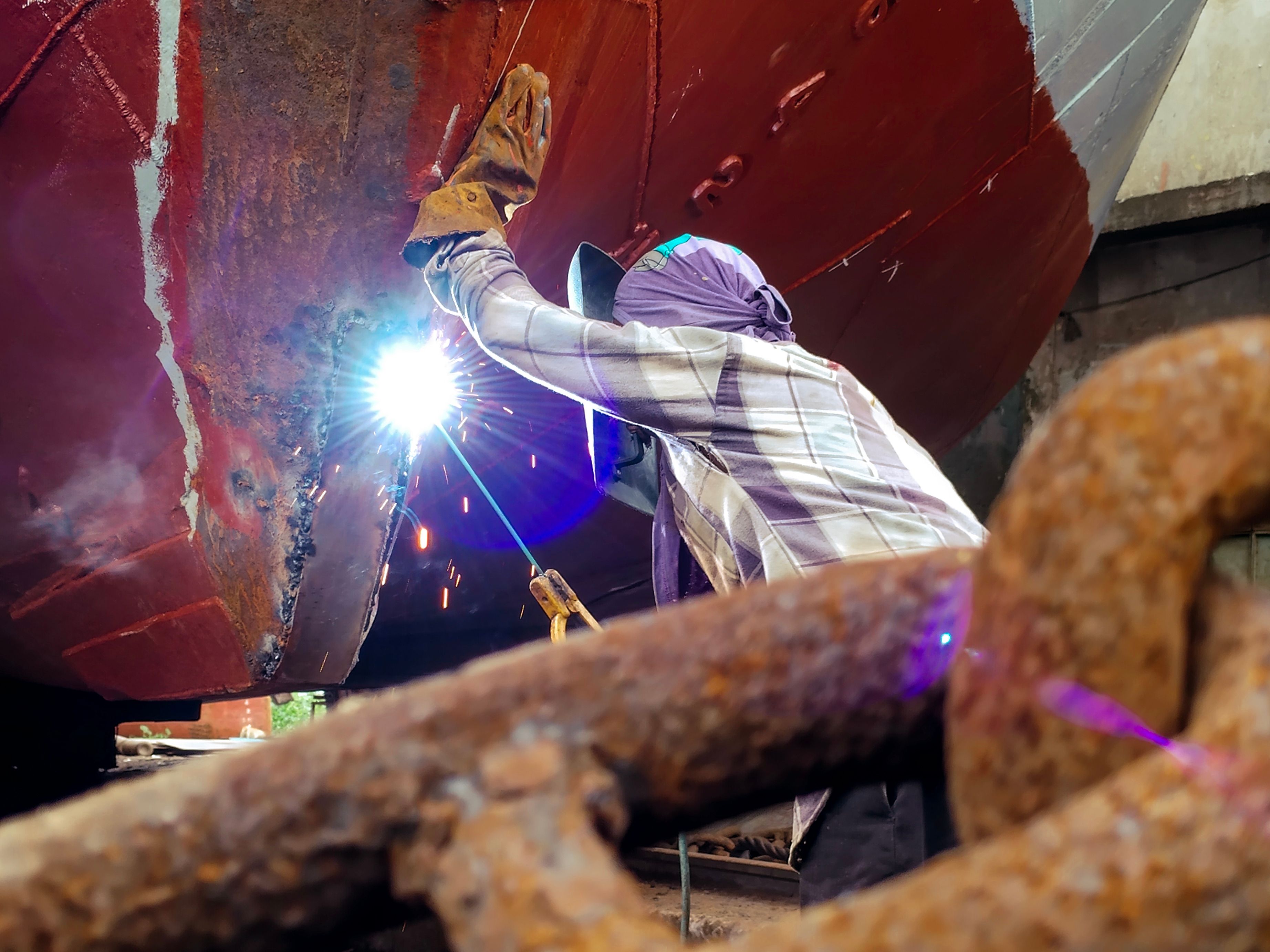 Shipyard worker welding a vessel hull