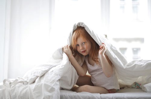 免费 孩子覆盖她的身体在白色的床罩 素材图片