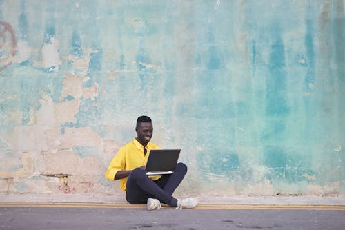 Man Sitting on Sidewalk Using Laptop