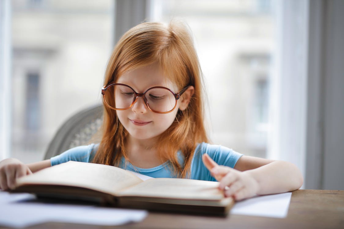 Girl in Blue Shirt Wearing Eyeglasses Reading Book