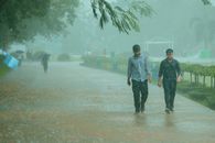 Two men stroll through a park pathway during a heavy rain shower, enjoying the rainy day.