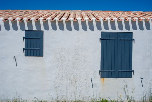 Exterior of a building with blue shutters, white walls, and red clay roof tiles under a clear sky.