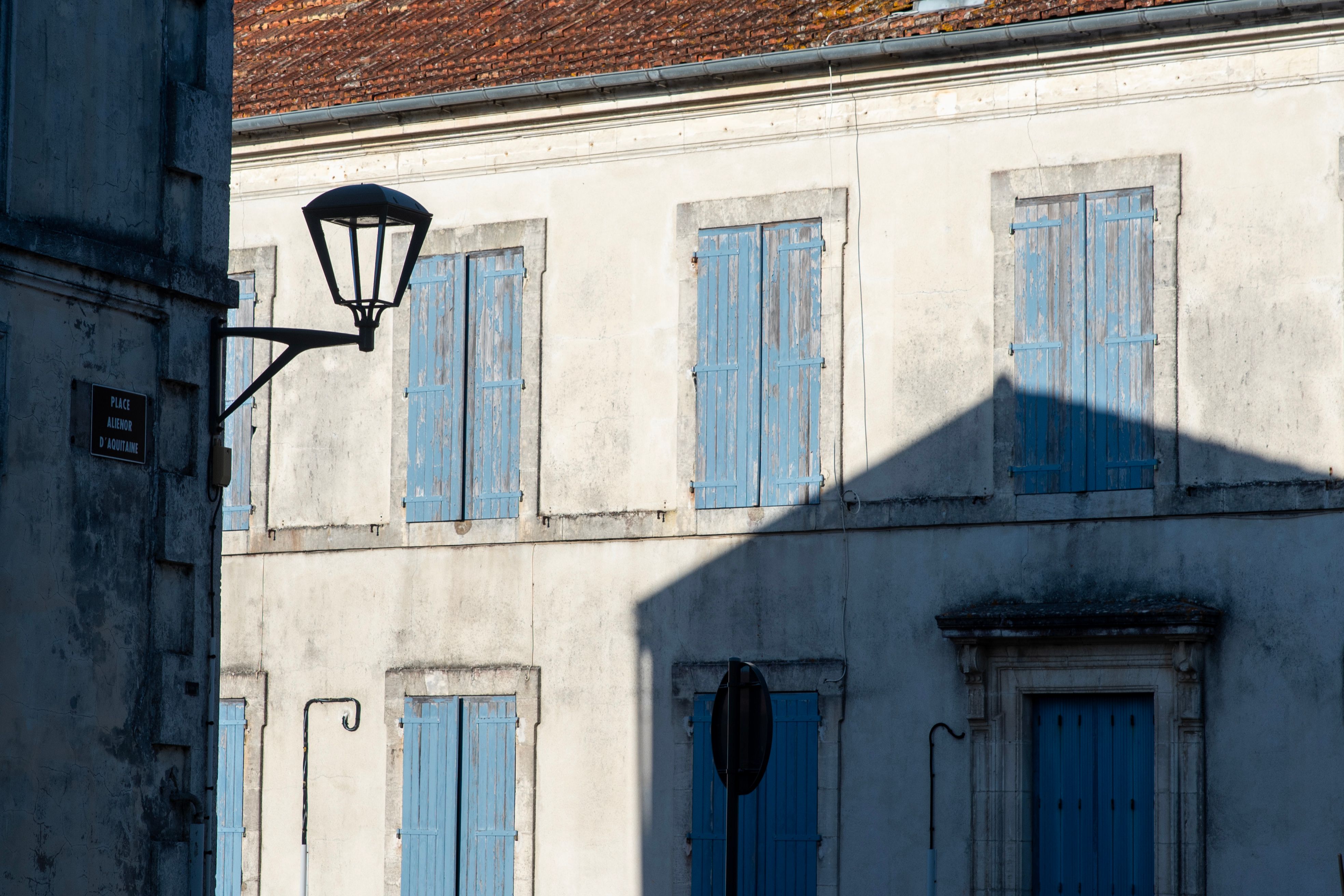 Sunlit facade with blue shutters casts shadows on a Saint-Georges-d'Oléron street