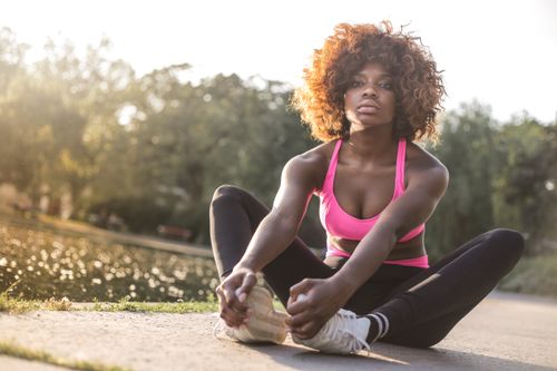 Free Black woman doing stretches outdoors in a pink sports bra on a sunny day. Stock Photo