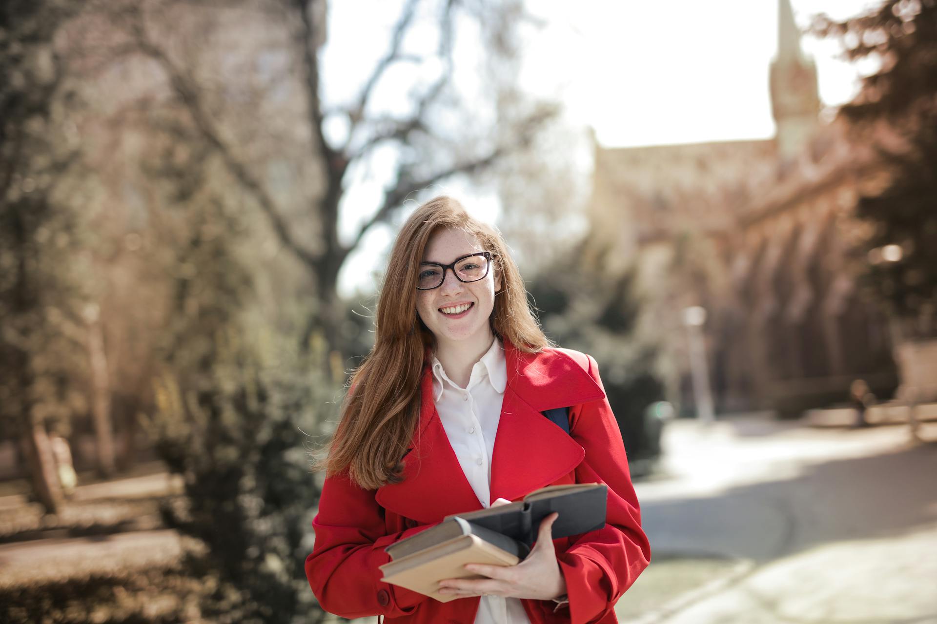 Smiling college student holding books in a park with a scenic background.