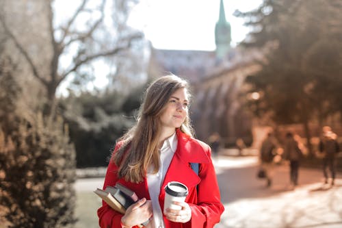 ノートブックとコーヒーカップを保持している赤いコートの女性