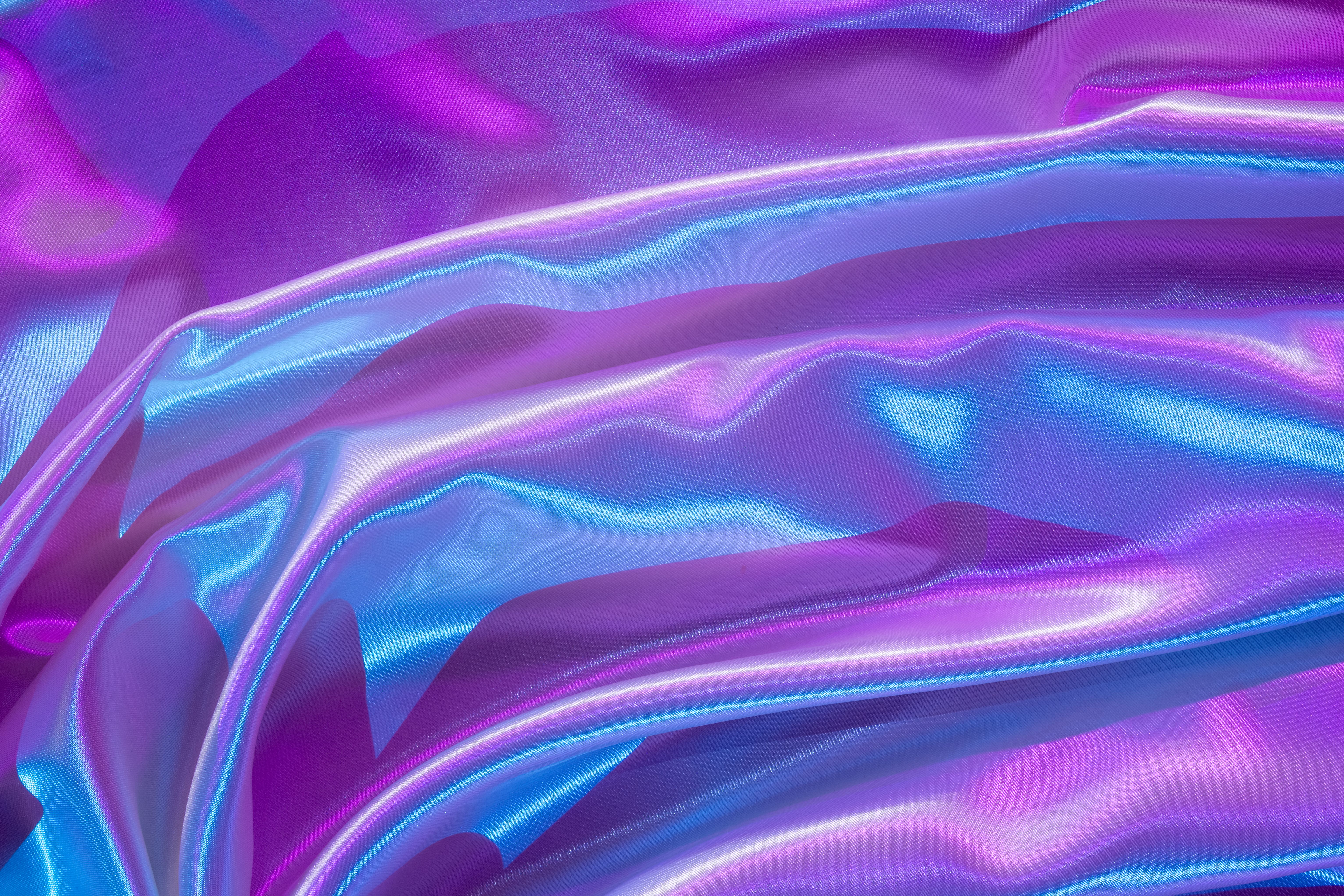 Iridescent satin fabric with purple and blue waves creates a modern, abstract background.