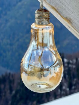 A vintage light bulb reflects a scenic mountain landscape, creating an artistic outdoor composition.