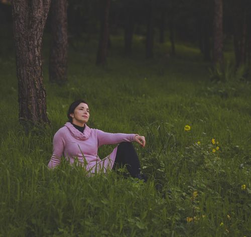 Free A serene image of a woman in a pink sweater relaxing on grass in a peaceful forest. Stock Photo