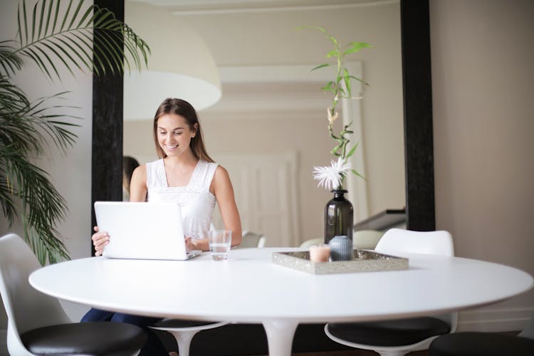 Woman In White Sleeveless Dress Sitting On Chair In Front Of Table With Macbook