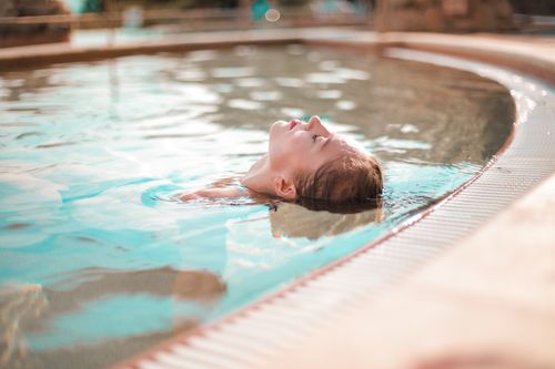 Free A woman enjoys peaceful relaxation while floating in a sunny outdoor pool, captured in soft natural light. Stock Photo