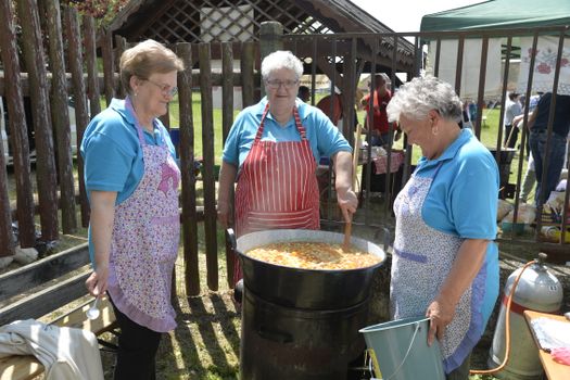 Three women prepare a traditional dish outdoors in Győrtelek, Hungary, showcasing cultural cooking techniques.