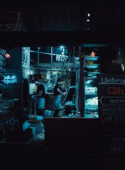 Side view faceless cafeteria staff in uniforms and aprons preparing orders while working at counter at night time