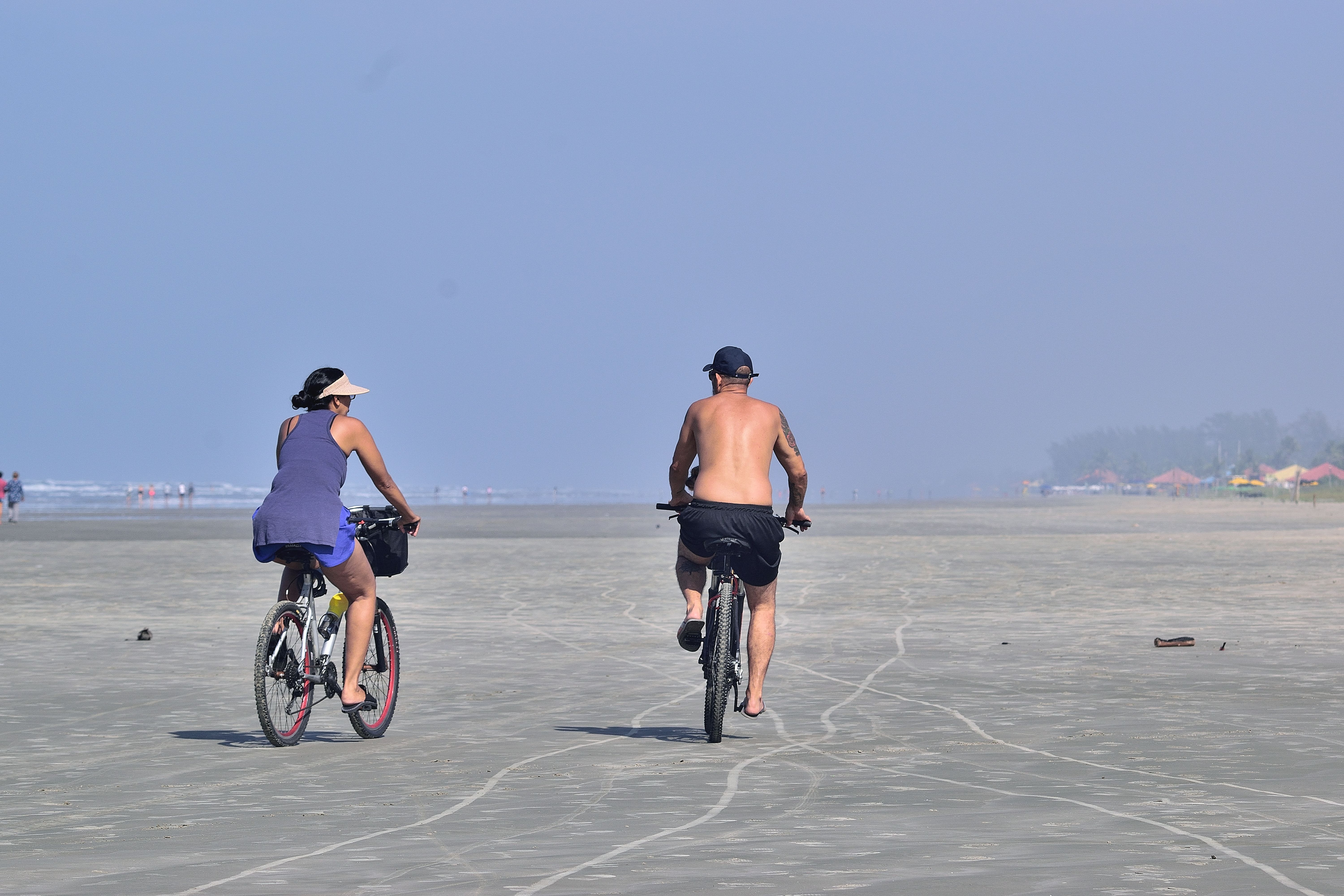 Two people cycling on Itanhaém Beach, São Paulo, enjoying a sunny day.