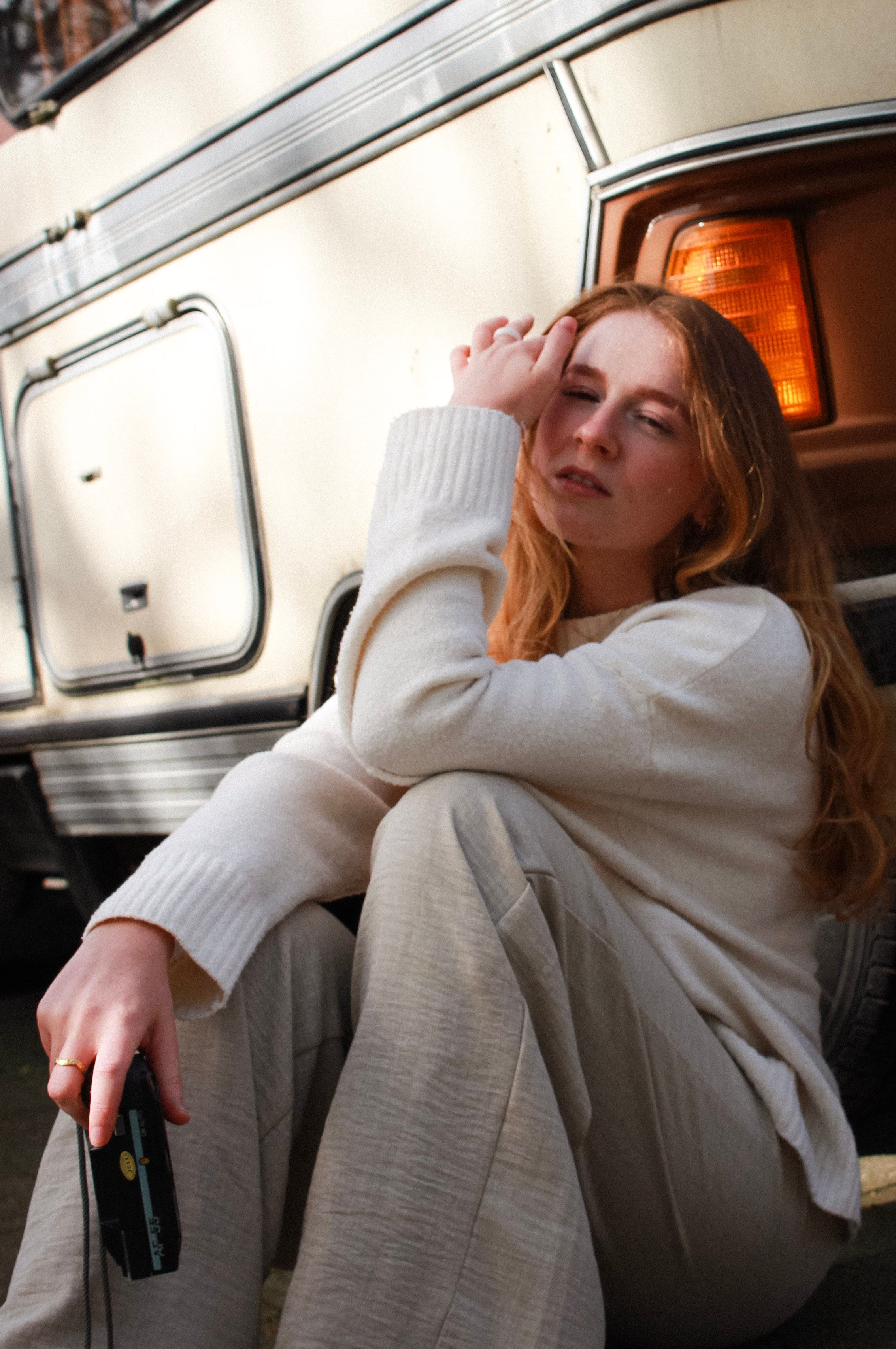 A serene moment of a young woman sitting by a campervan in sunlight, creating a warm and peaceful vibe.