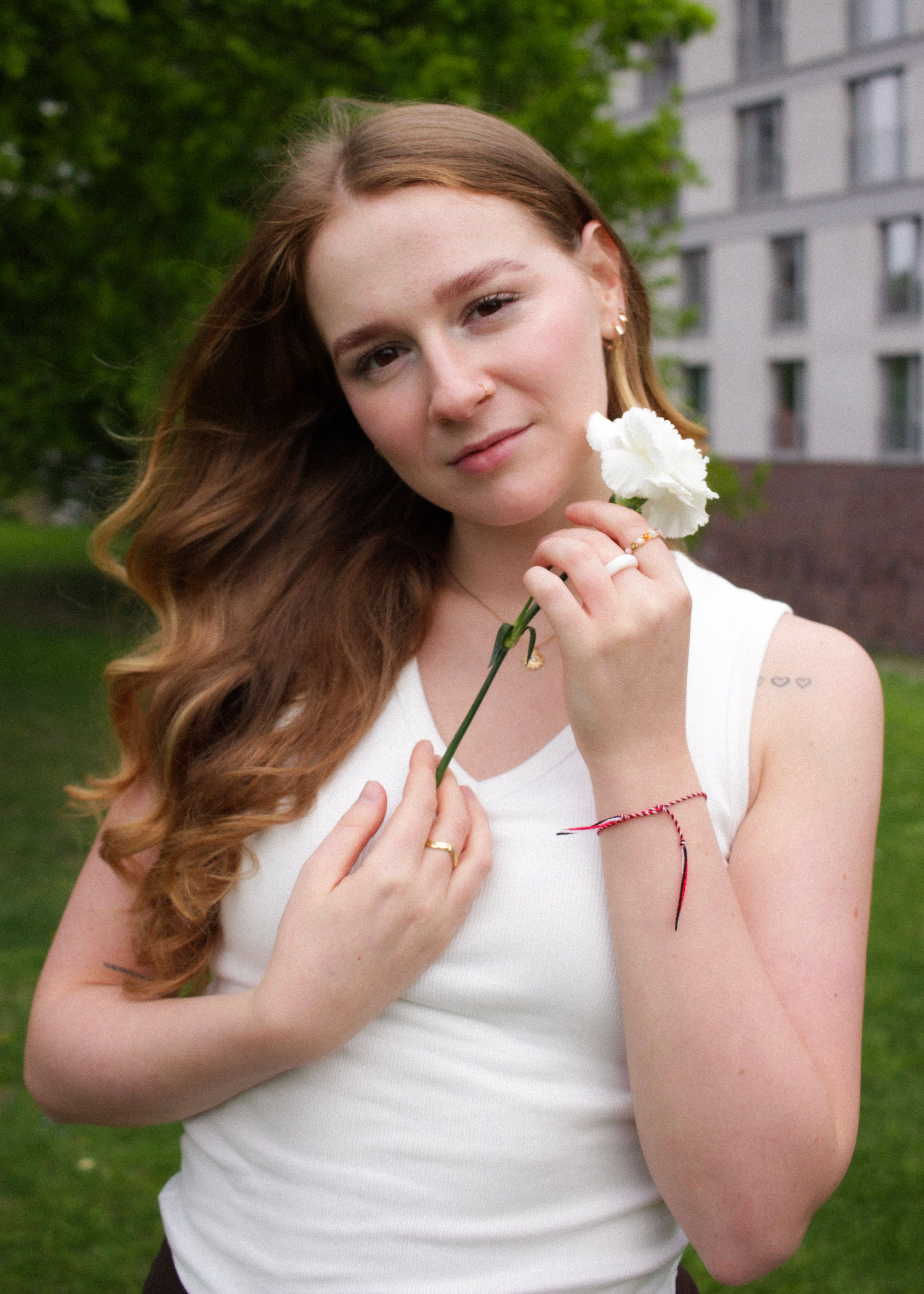 A woman enjoying nature, holding a white flower outdoors in a park.