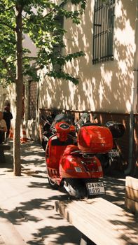A vibrant red Vespa scooter parked on a tree-lined street during the day.