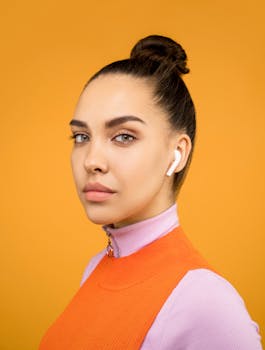 橙色背景下的时尚女士搭配无线耳机，尽显现代风格