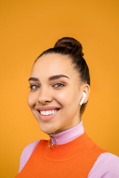 在橙色背景下，一位戴着无线耳机的年轻女子微笑着，肖像明亮而欢快