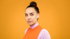 一位时尚女性戴着耳塞的肖像，以充满活力的橙色为背景，展现了现代时尚