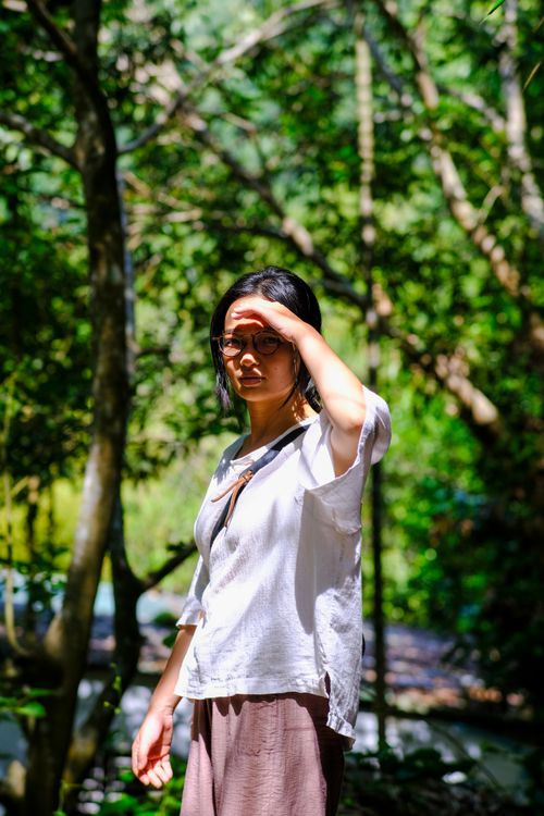 Free Portrait of a young woman shielding her eyes from the sun in a lush forest in Da Nang, Vietnam. Stock Photo