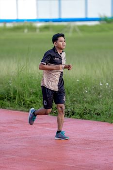 Man jogging on a red track surrounded by greenery, promoting fitness and health.