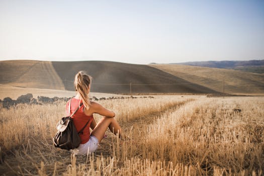 Woman sitting with backpack in rural wheat field, enjoying serene summer landscape.