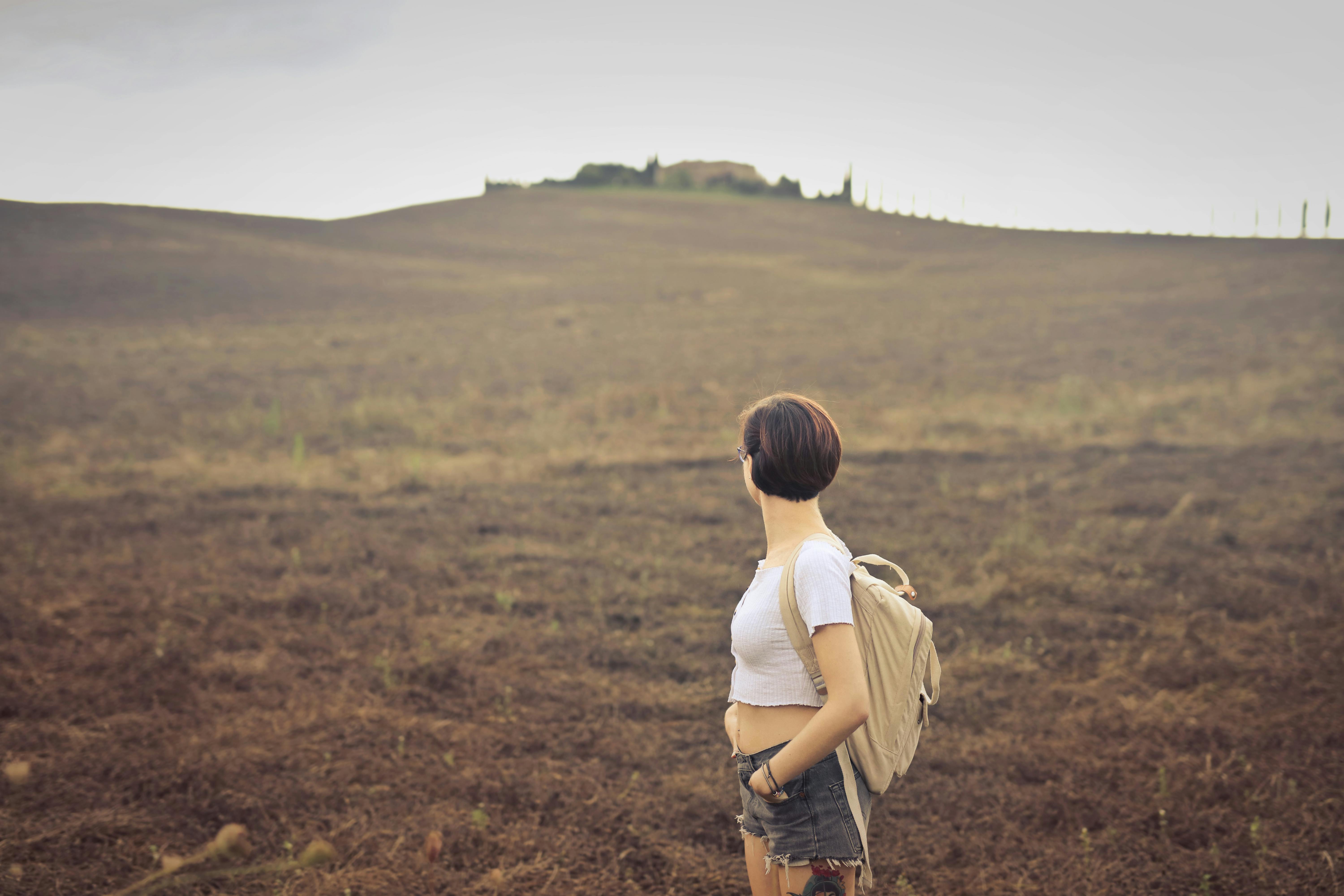 一位背着背包的女人，站在广阔的乡村田野上，显得孤独