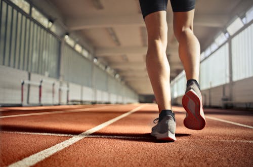 Free From below back view of crop strong runner walking along running track in athletics arena while doing warm up exercises during workout Stock Photo