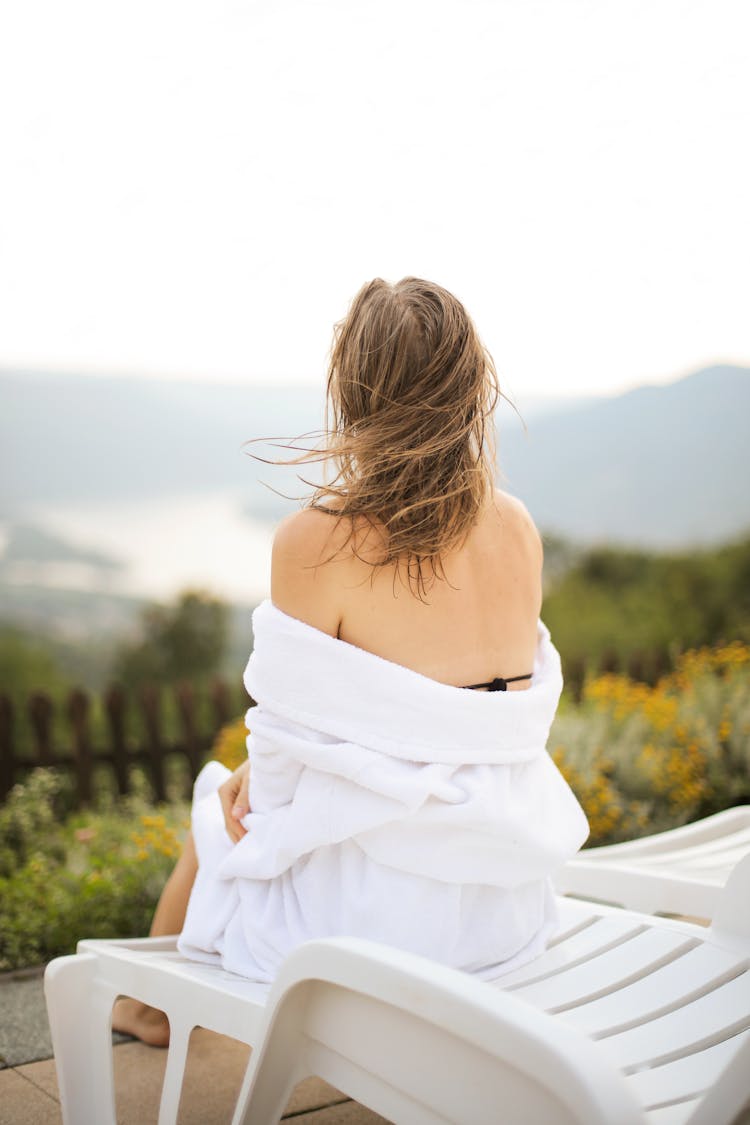  Back View Photo Of Woman In White Robe Sitting On White Pool Chair