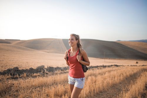 Free Smiling woman in casual attire enjoying a summer hike through golden fields at sunset. Stock Photo