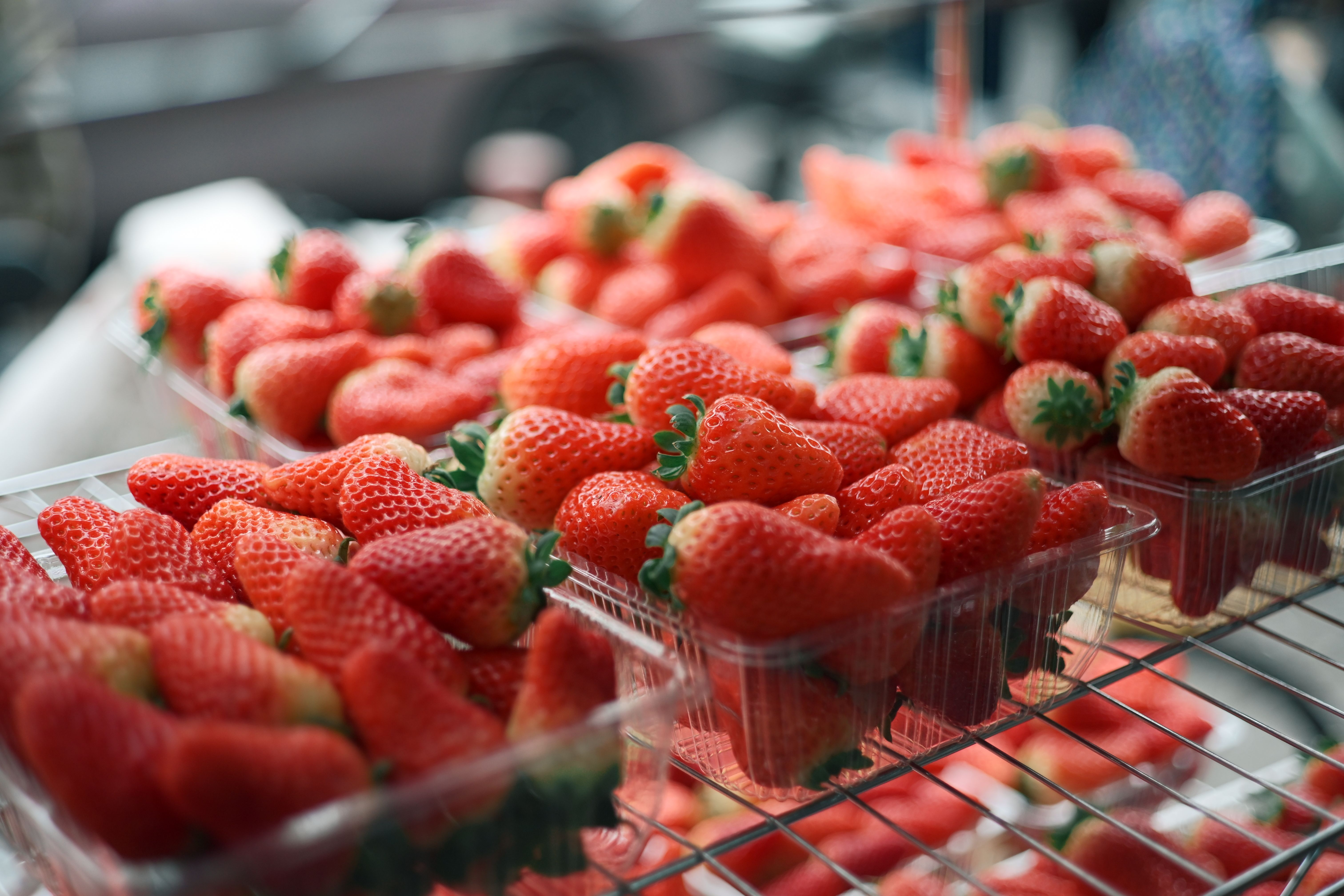 Bright red strawberries in plastic containers at an outdoor market stand.