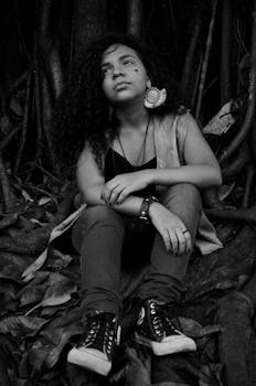 一位穿着休闲装、神情深思的女人坐在树根之间，显得孤独而沉静