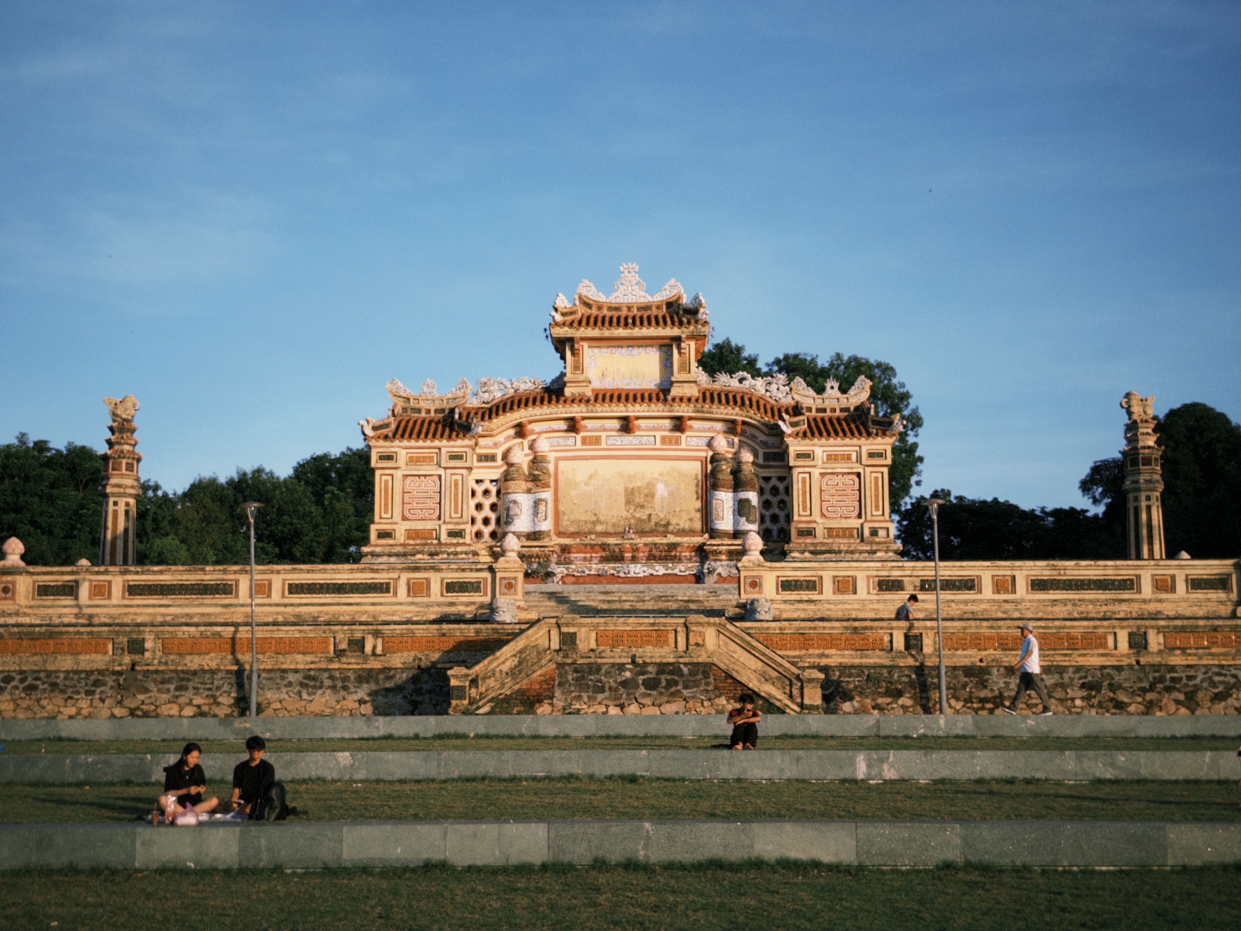 A beautiful Vietnamese temple at sunset with people relaxing on the lawn, showcasing traditional architecture.