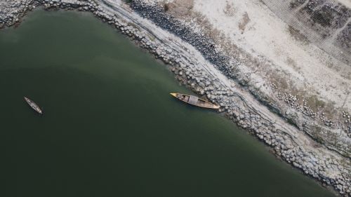 Free Aerial shot of wooden boats near a rocky shore on a calm green river. Stock Photo