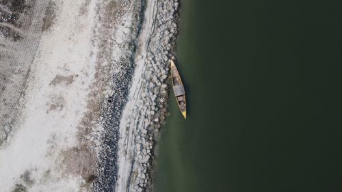 Free Aerial shot of a solitary wooden boat on a rocky riverbank with green water. Stock Photo
