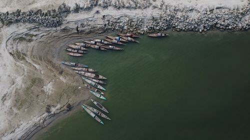 Free Aerial view of traditional wooden boats moored along a muddy riverbank in a serene setting. Stock Photo
