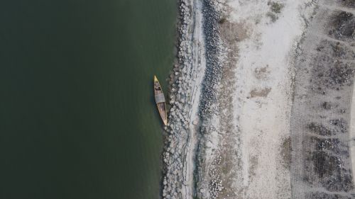 Free Aerial view capturing a lone boat by a rocky riverbank with green water. Stock Photo