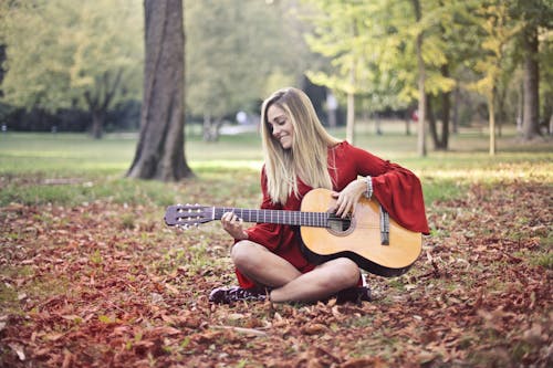 Woman in Red Long Sleeve Dress Playing Brown Acoustic Guitar Sitting on the Ground