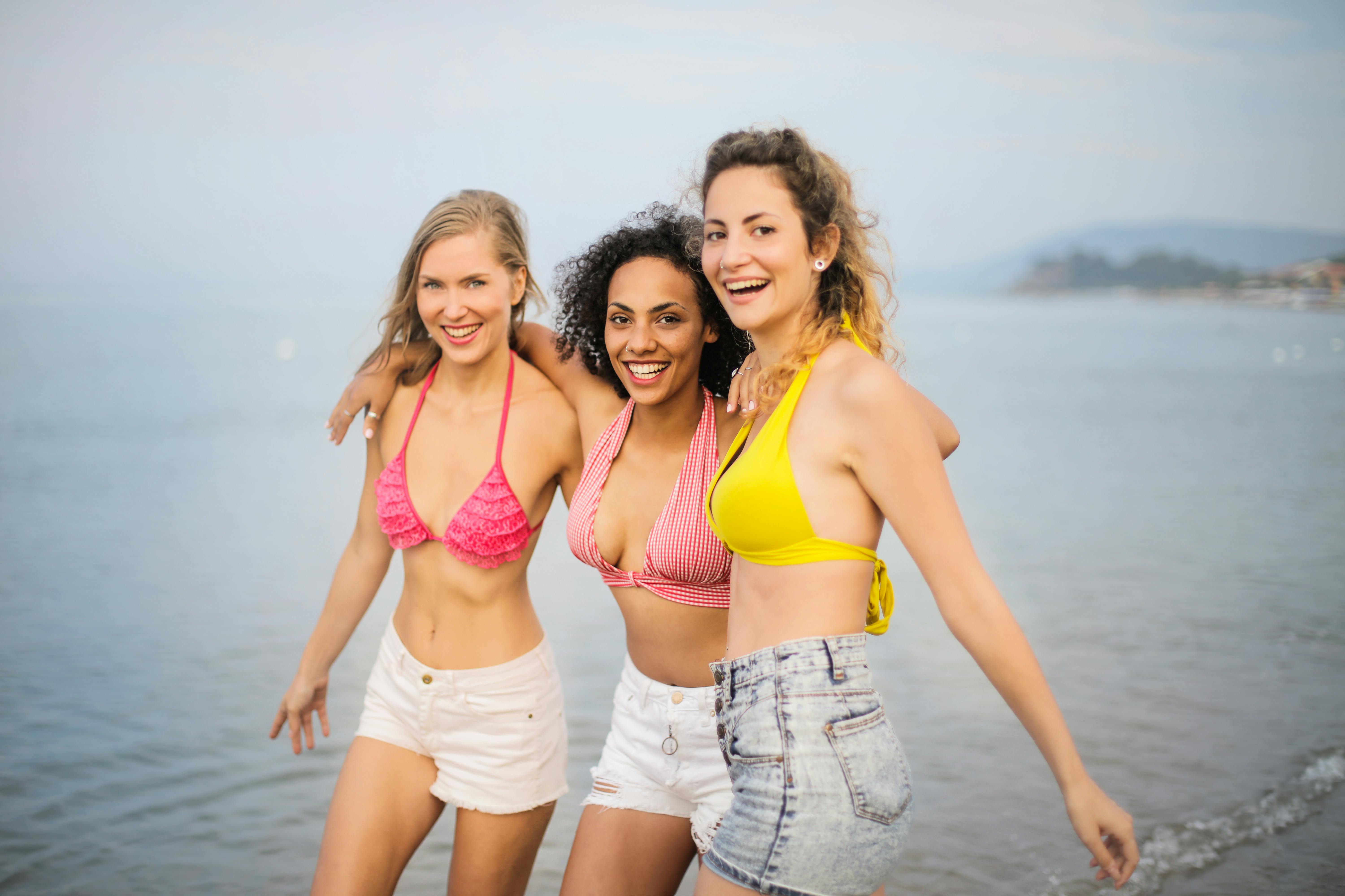 Beautiful girl in beige bikini and denim shorts standing with big green  leaves on background Stock Photo by garetsworkshop