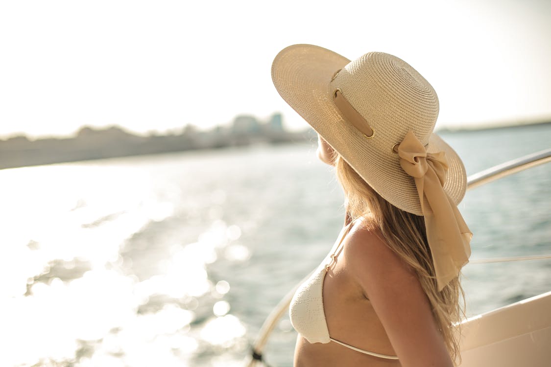 Free Back view of slim female in bikini top and straw hat enjoying trip on cruise boat on sunny day while relaxing during summer vacation and looking away Stock Photo