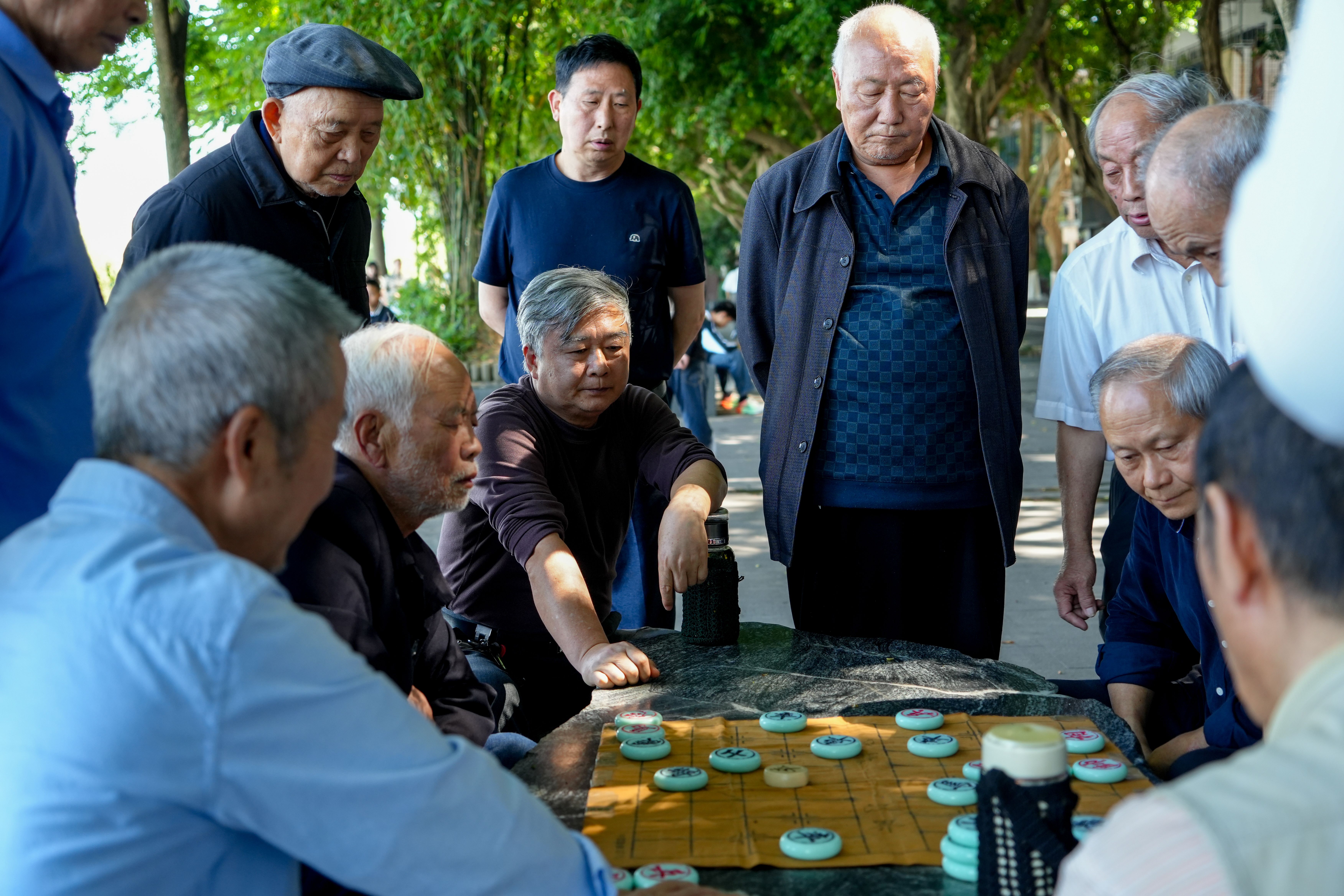 Group of senior men engaged in a game of Xiangqi in an outdoor park setting.