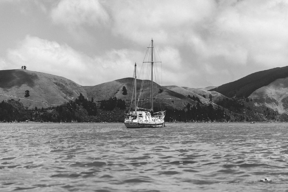 A tranquil view of a sailboat on the waters of Marlborough Sound, New Zealand, with rolling hills in the background.