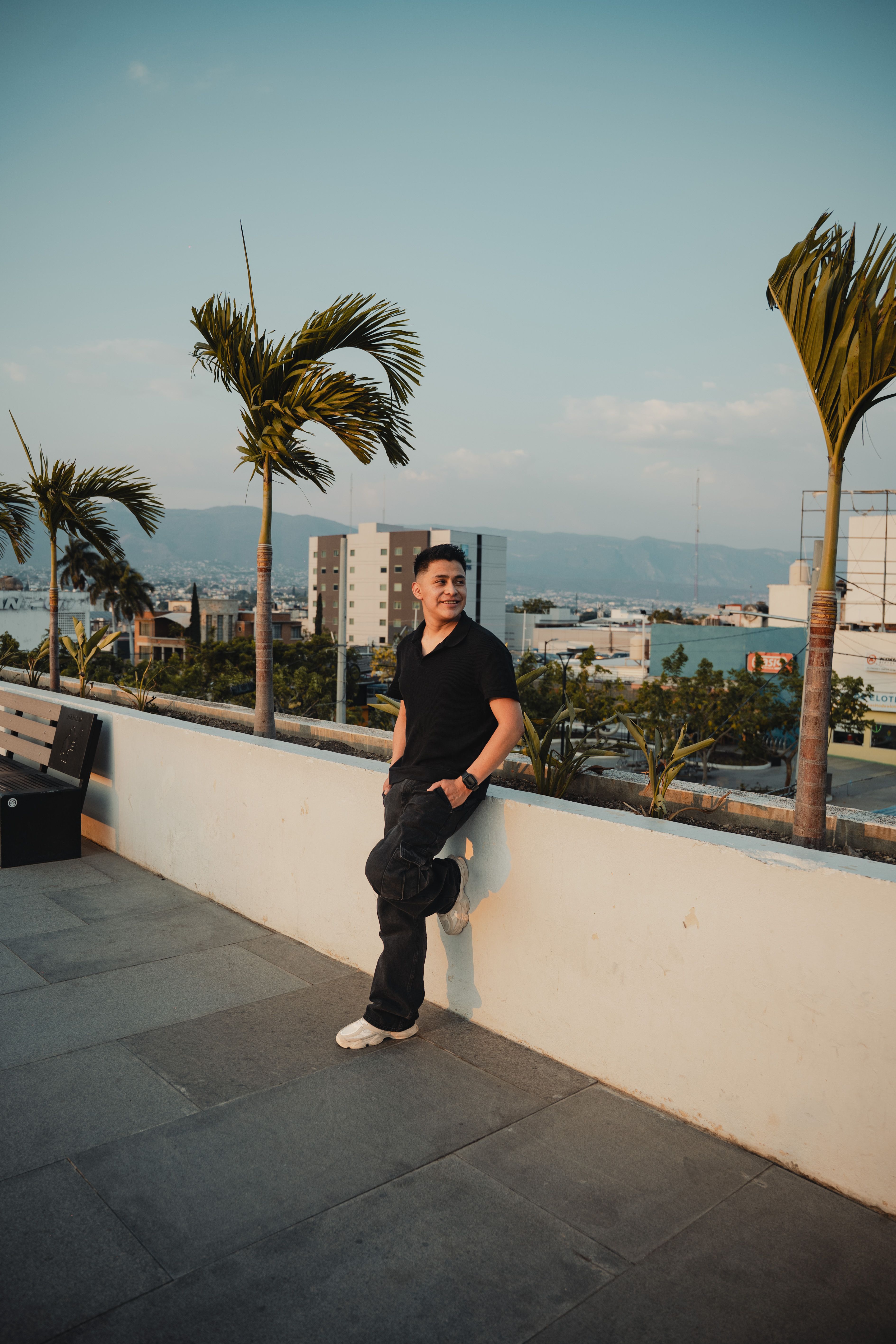 Man standing on a rooftop with palm trees and city view in Tuxtla Gutiérrez, Mexico.