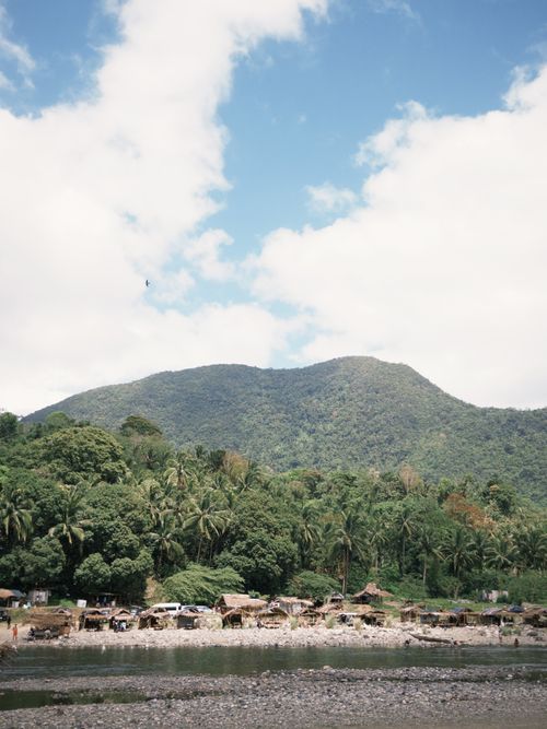 Free Scenic view of a mountain with lush greenery and a quaint riverside village under a blue sky. Stock Photo