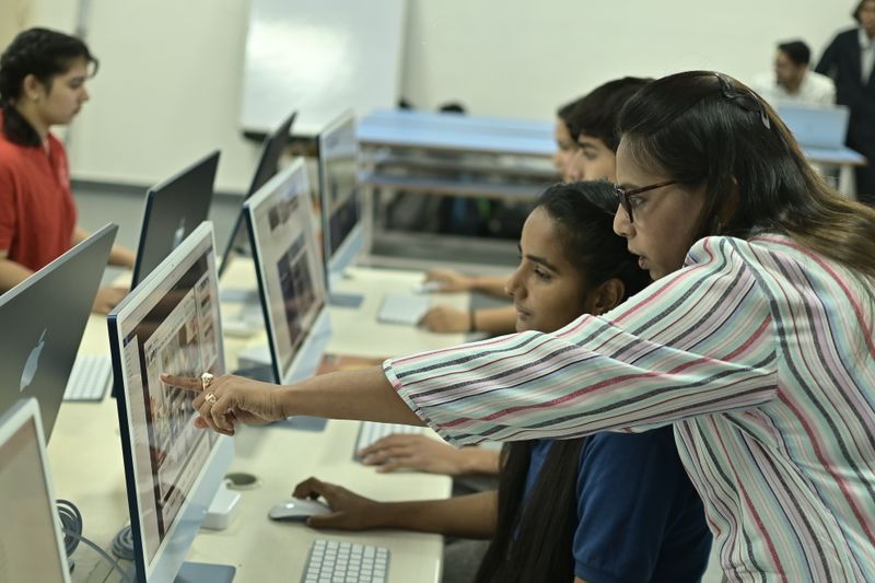 Students and a teacher working together at workstations in an institutional computer laboratory