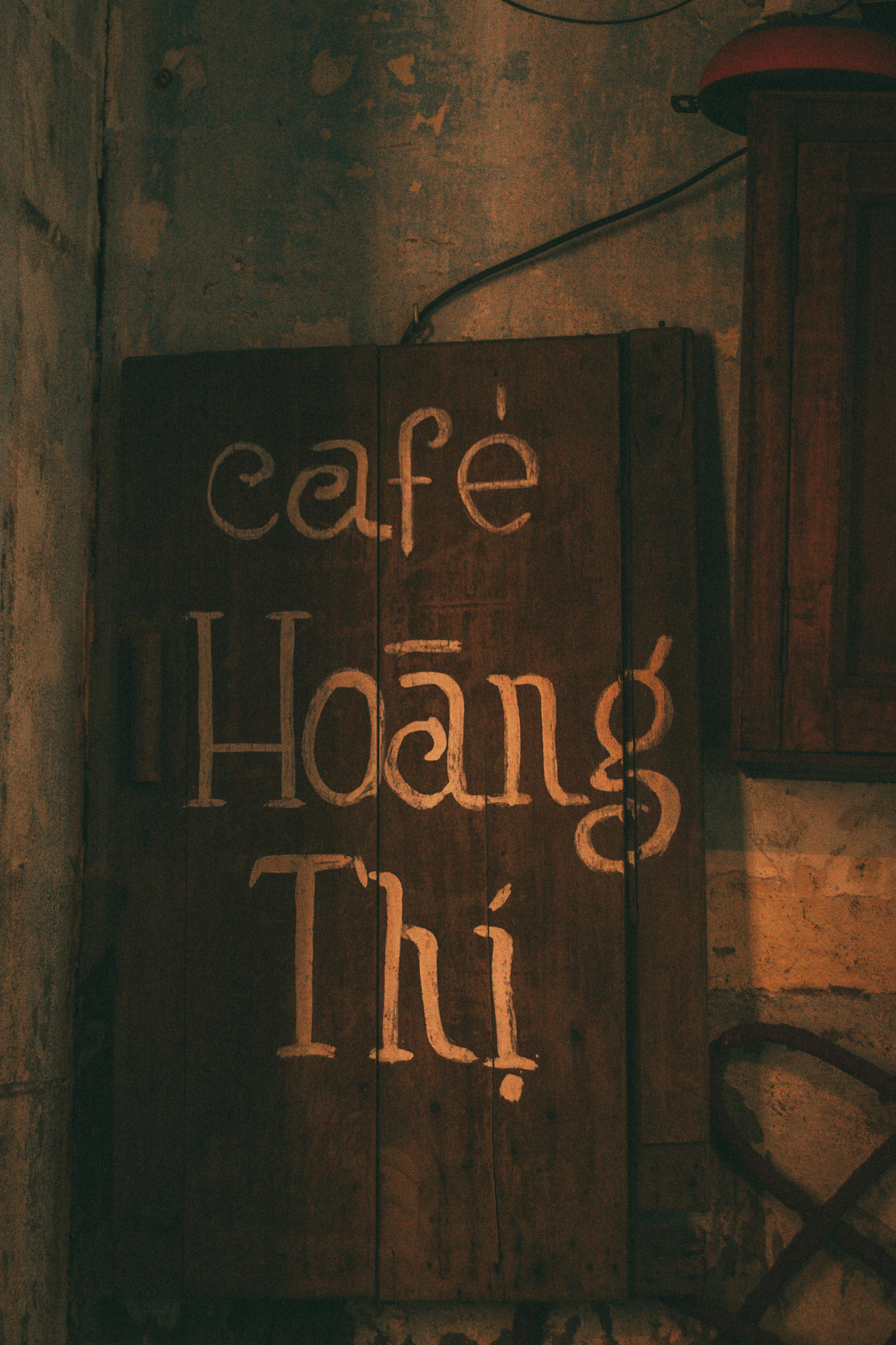 Vintage wooden cafe sign 'Hoàng Thị' with rustic charm against a textured background.