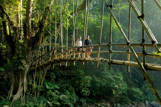 Two people walking across a bamboo bridge in a lush green jungle in Banten, Indonesia.